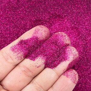 May include: A hand holding a pile of fine pink glitter. The glitter is very sparkly and has a metallic sheen.