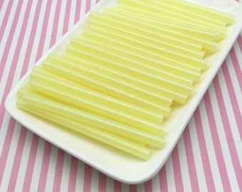 May include: A white plate filled with yellow glitter glue sticks. The glue sticks are arranged in a neat, overlapping pattern.