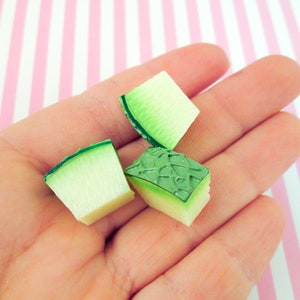 May include: Three green and white plastic watermelon slices. The slices are in the palm of a hand.