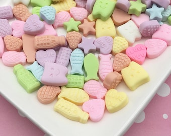 May include: Assortment of pastel-colored candy shaped like hearts, stars, fish, and other cute designs. The candy is arranged on a white plate with a pink polka dot background.