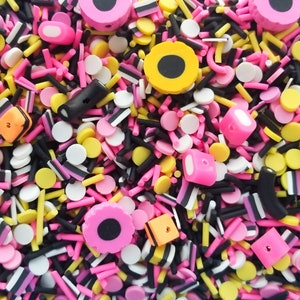 May include: A variety of colorful sprinkles and candy pieces, including black and white licorice, pink and yellow candy circles, and black and white striped candy sticks.
