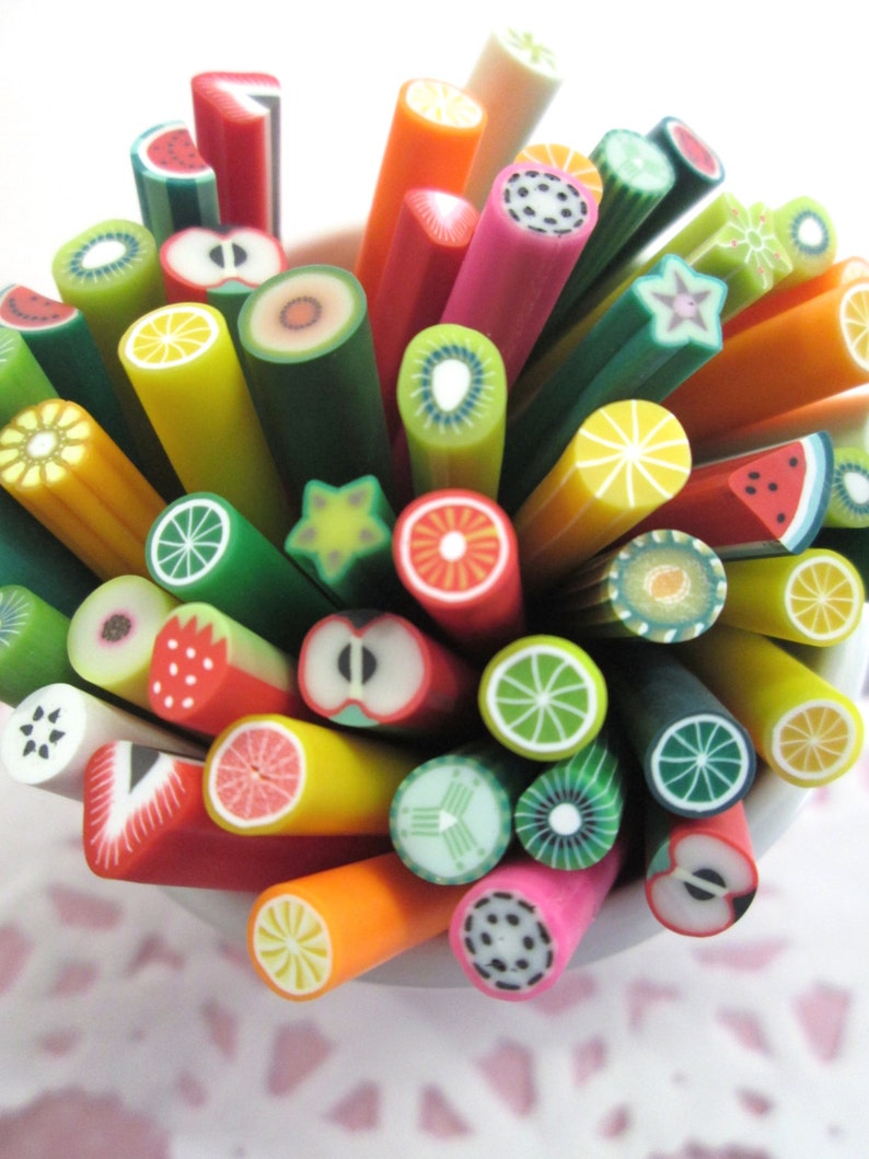 May include: A collection of colorful polymer clay fruit slices, each with a different design, arranged in a white bowl. The slices include watermelon, kiwi, lemon, lime, apple, strawberry, and more.