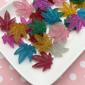 May include: Assortment of glitter leaf shaped resin embellishments in various colors, including pink, purple, blue, green, gold, and silver.