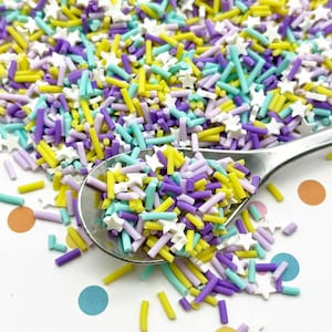 Könnte beinhalten: Nahaufnahme eines Löffels gefüllt mit bunten Streuseln. Die Streusel sind eine Mischung aus Gelb, Lila, Blau und Weiß. Die Streusel haben die Form von Sternen und langen, dünnen Stäbchen.