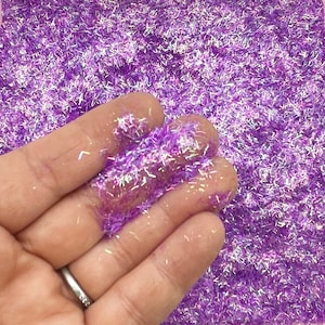 May include: Purple iridescent glitter with a holographic finish. The glitter is in a loose, fine texture.