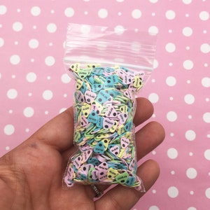 May include: A clear plastic bag filled with colorful heart-shaped sprinkles. The sprinkles are decorated with black dots and the words "OUIJA" and "ALIJO" printed on them.