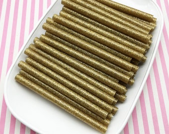 May include: A white plate filled with gold glitter glue sticks. The glue sticks are arranged in a neat stack.