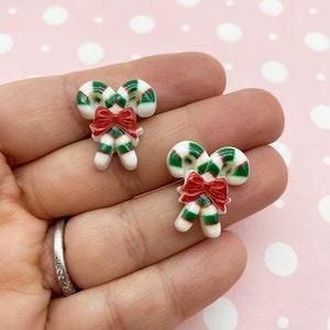 May include: Two white, green, and red candy cane ornaments with a red bow. The ornaments are made of resin and are perfect for adding a festive touch to your Christmas decor.
