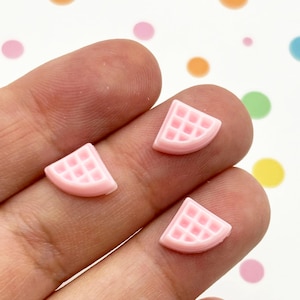 May include: Three pink waffle-shaped resin earrings. The earrings are shaped like a slice of waffle and have a textured surface.