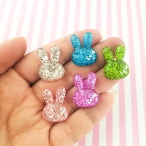 May include: Five glitter bunny charms in different colours: silver, blue, green, pink, and light pink. Each charm has the word "Love" written on it.