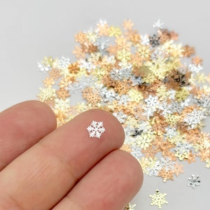 A hand holding a small silver snowflake against a background of various colored snowflake-shaped objects.
