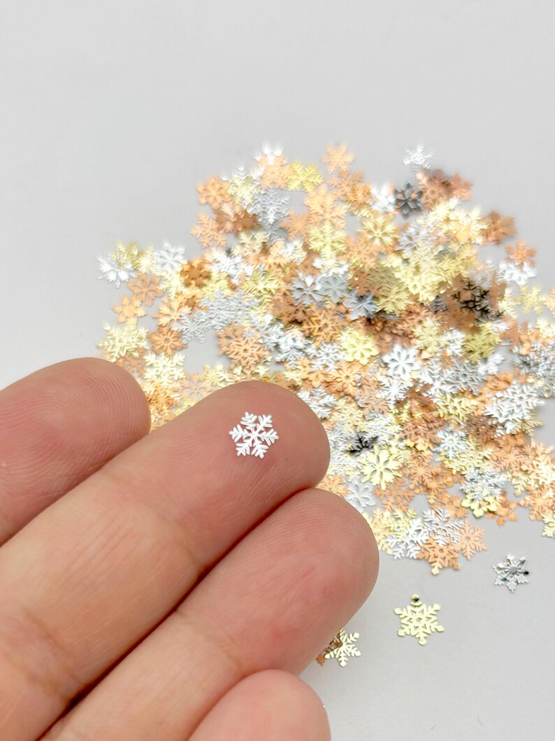 A hand holding a small silver snowflake against a background of various colored snowflake-shaped objects.