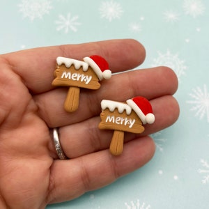 May include: Two small brown wooden signs with white "Merry" lettering and a red Santa hat on top.