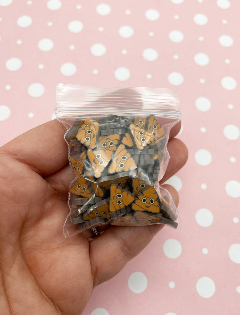 May include: A clear plastic bag filled with small brown and grey resin poop emoji charms. The charms have a smiley face with two black eyes.