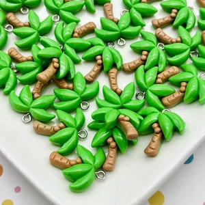 May include: A collection of green palm tree charms with brown trunks and silver jump rings. The charms are arranged on a white surface, creating a tropical theme. These small, detailed charms are suitable for jewelry making or craft projects.
