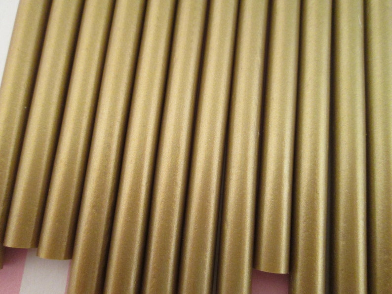 Op de afbeelding: Een close-up van een bundel goudkleurige wasstokken. De stokken zijn in een rij gerangschikt en zijn allemaal even groot en even gevormd.
