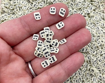 May include: A close-up of a hand holding a variety of white and black ghost-shaped sprinkles. The sprinkles are small and have a black outline and eyes.