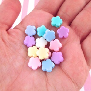 Puede incluir: Una colecci&oacute;n de cuentas de pl&aacute;stico con forma de flor de color pastel. Las cuentas son de color rosa, azul, amarillo y blanco.