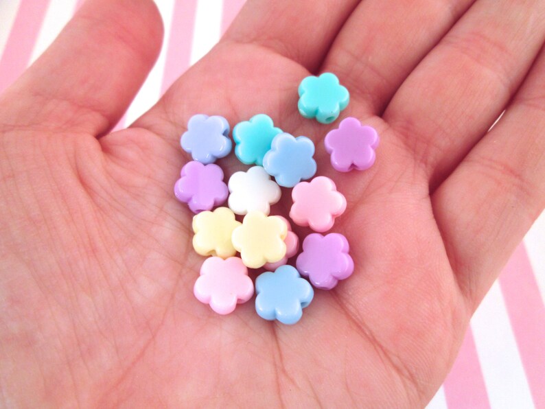 Puede incluir: Una colecci&oacute;n de cuentas de pl&aacute;stico con forma de flor de color pastel. Las cuentas son de color rosa, azul, amarillo y blanco.
