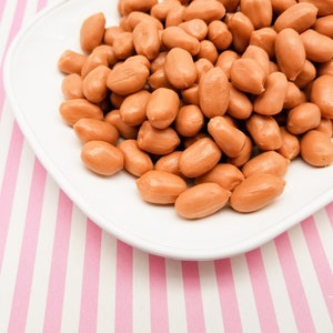 May include: A white plate filled with small, light brown sausages on a pink and white striped background.
