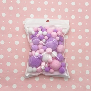 May include: A clear plastic bag filled with a variety of small, fluffy pom-poms in white, pink, and purple.