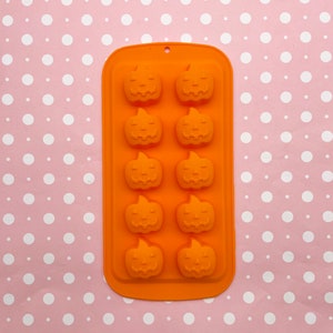 Könnte beinhalten: Orangefarbene Silikonform mit 10 Vertiefungen in Form von Kürbissen. Die Form ist zum Herstellen von Süßigkeiten, Schokolade oder anderen Leckereien gedacht.