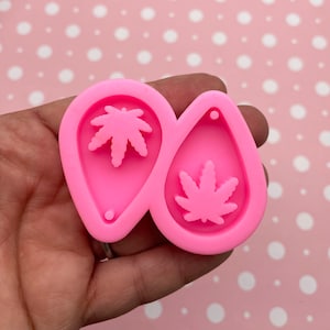 Puede incluir: Molde de silicona rosa para hacer pendientes de resina. El molde tiene dos cavidades en forma de lágrima con un pequeño agujero en la parte superior para un aro de salto. Cada cavidad presenta un diseño de hoja de marihuana en relieve.