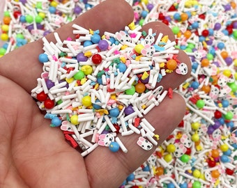 Pode incluir: Uma variedade de confeitos coloridos, incluindo varetas brancas, bolas redondas e pequenas faces de coelho. Os confeitos estão em uma mão, prontos para serem usados para decorar.