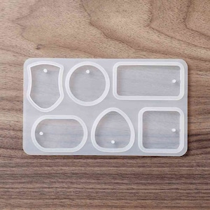 May include: A clear silicone mold with six different shapes for making jewelry or other crafts. The shapes include a shield, a circle, a rectangle, an oval, and two squares.