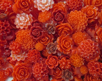May include: Assortment of orange and red resin flower embellishments. The flowers are in various shapes and sizes, including roses, daisies, and other floral designs.