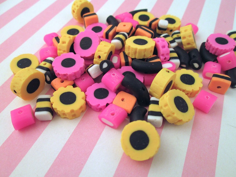 May include: A collection of colorful candy-themed polymer clay beads in black, yellow, pink, and white. The beads are shaped like licorice, jelly beans, and other candies.