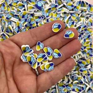 May include: A large quantity of small, white, blue, and yellow firefly charms. The charms are made of polymer clay and have a flat back. They are perfect for adding a touch of whimsy to crafts and jewelry.