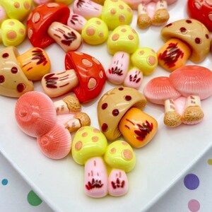 May include: A selection of mushroom-shaped charms in a variety of colours and designs. The charms feature shades of red, yellow, pink, and brown, with detailed caps and stems. Some have polka dots, and others have intricate patterns.