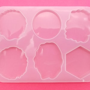 May include: A pink silicone mold with six different shapes for resin casting. The shapes include a circle, a hexagon, and four irregular shapes.