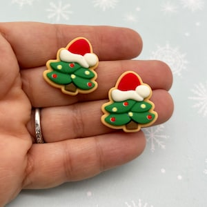 May include: Two Christmas tree-shaped cookie charms with red and white Santa hats, green frosting, and yellow lights. The charms are made of polymer clay and are approximately 1 inch in size.