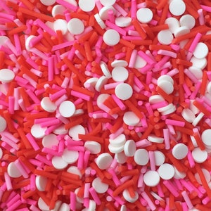 May include: A mix of red, pink, and white sprinkles. The sprinkles are in the shape of small cylinders and round discs.