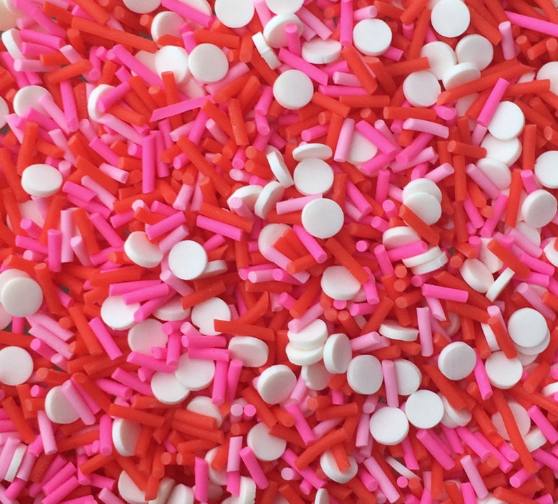 May include: A mix of red, pink, and white sprinkles. The sprinkles are in the shape of small cylinders and round discs.