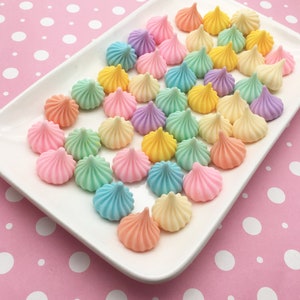 May include: A white plate filled with pastel-colored candy shaped like small, pointed cones. The candy is arranged in rows and is on a pink background with white polka dots.