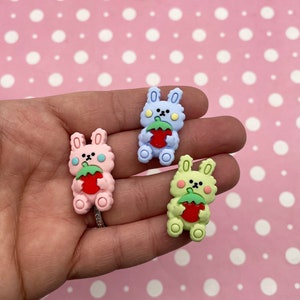 May include: Three small, colourful bunny-shaped charms with a strawberry design. The bunnies are light blue, pink, and green.