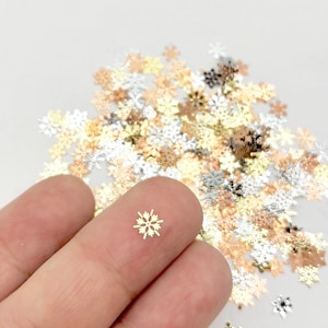 A hand holding a small, golden snowflake-shaped object against a background of scattered, colorful snowflake-shaped objects.