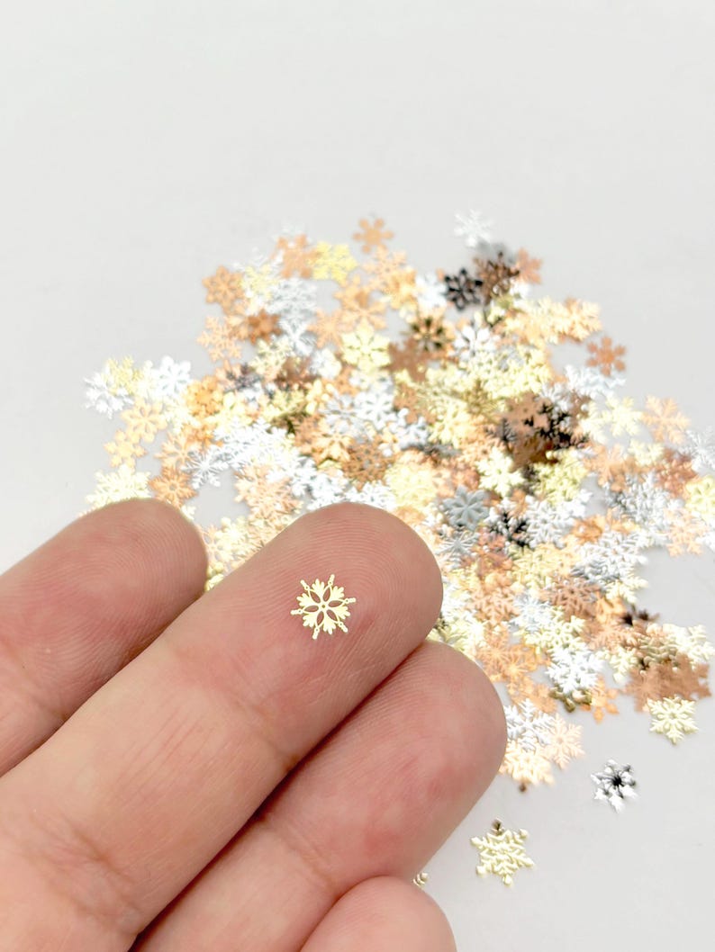 A hand holding a small, golden snowflake-shaped object against a background of scattered, colorful snowflake-shaped objects.