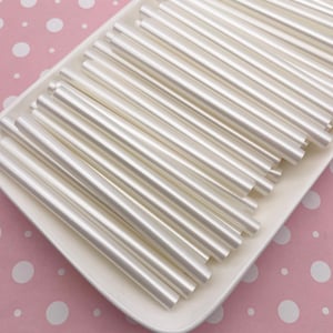 May include: A white plate filled with a stack of white, opaque, round, plastic rods. The rods are arranged in a neat, overlapping pattern.
