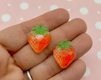 May include: Two red and white strawberry shaped resin cabochons with green leaves.