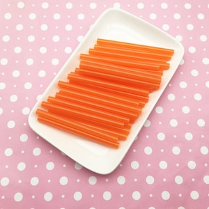 May include: A white rectangular plate filled with a stack of orange plastic drinking straws.