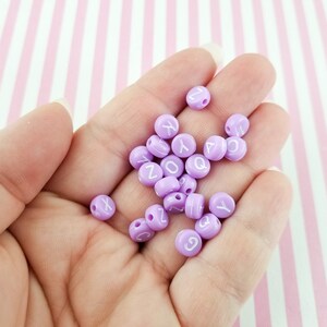 Peut inclure: Un ensemble de perles d'alphabet violettes avec des lettres blanches. Les perles sont rondes et ont un trou au centre pour &ecirc;tre enfil&eacute;es.