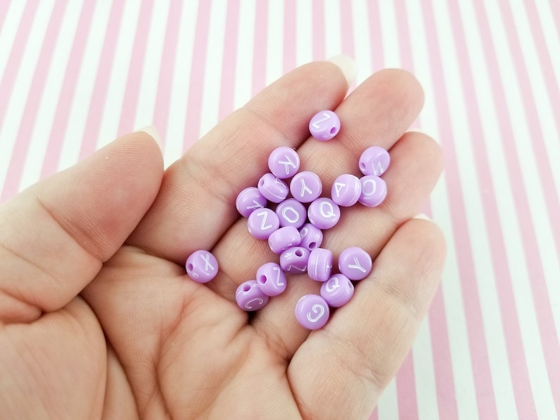 Peut inclure: Un ensemble de perles d'alphabet violettes avec des lettres blanches. Les perles sont rondes et ont un trou au centre pour &ecirc;tre enfil&eacute;es.