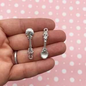Puede incluir: Dos encantos de cuchara de plata con detalles ornamentados. Las cucharas tienen un cuenco redondeado y un mango decorativo. Los encantos tienen un lazo en la parte superior para sujetar a joyas u otras artesanías.