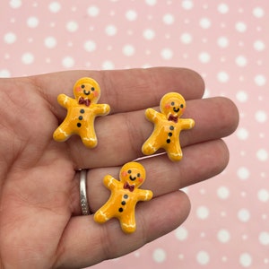 May include: Three small gingerbread man figurines with white icing and red bow ties. The gingerbread men are yellow and have black eyes and a black button.