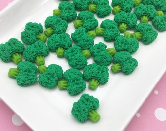 May include: A white plate with a large quantity of green broccoli-shaped embellishments. The plate is on a pink background with white polka dots.