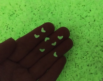 Könnte beinhalten: Nahaufnahme einer Hand mit mehreren kleinen, leuchtenden, herzförmigen Dekorationen. Der Hintergrund ist mit einem strukturierten, hellgrünen Material gefüllt. Die Herzen sind ein hellerer Grünton.